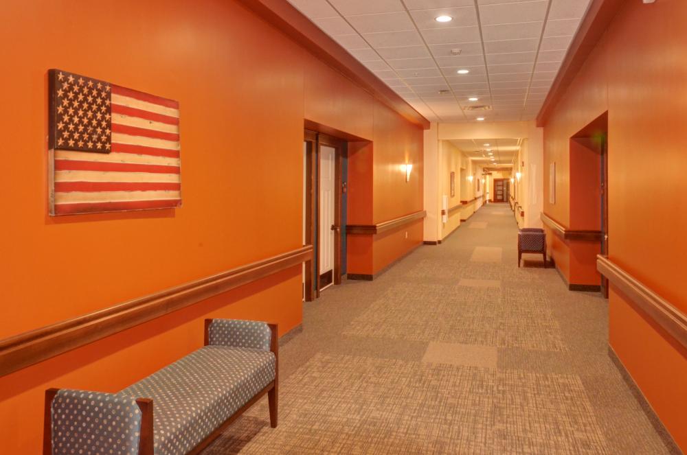 Interior hallway at Stillwater Senior Living in Edwardsville, Il. The warm colors follow evidence-based design conventions for nursing home design. Low railings are helpful for those with disabilities. 