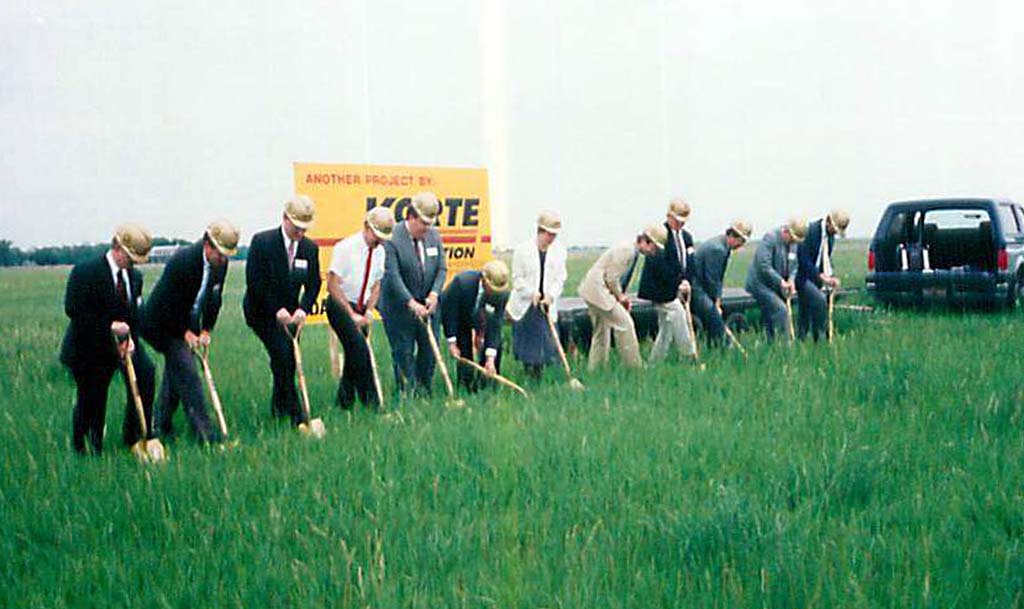 A group of people in hardhats with shovels break ground for a construction project.
