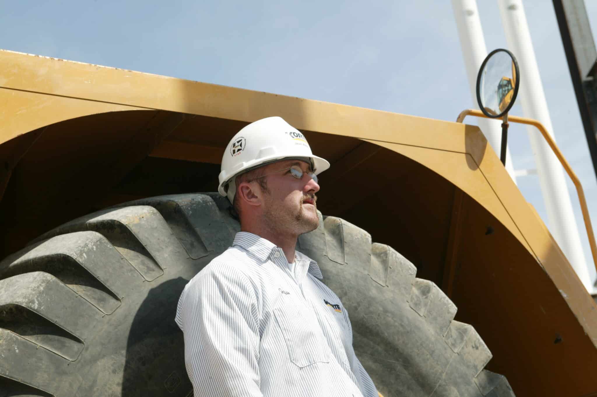 Man in a hardhat leaning against a heavy duty tire
