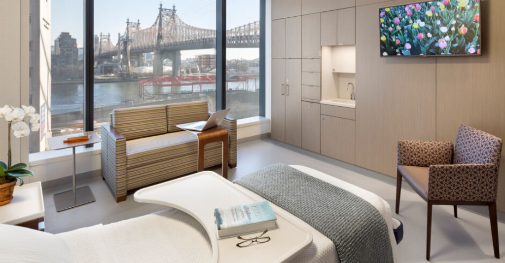 A patient room with a large picture window overlooking a waterfront.