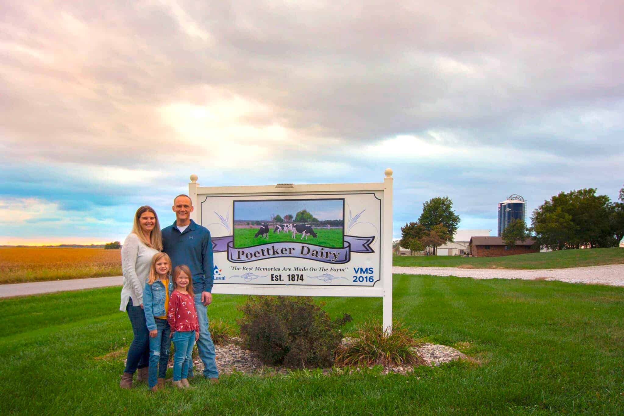 Nicole and family standing in front of family dairy century farm sign that reads, "Poettker Dairy."