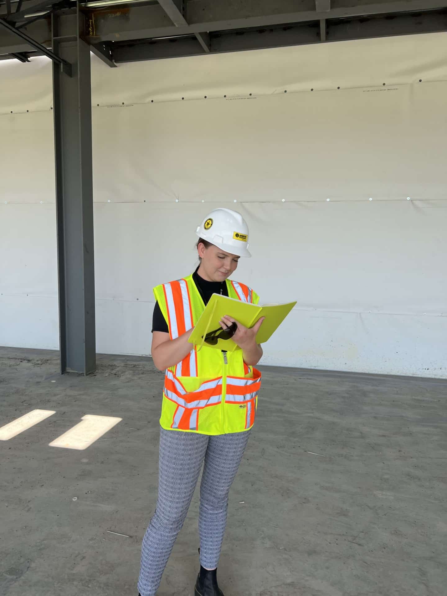 Macy Morley in a yellow safety vest and hard hat examining a file folder on a job site.