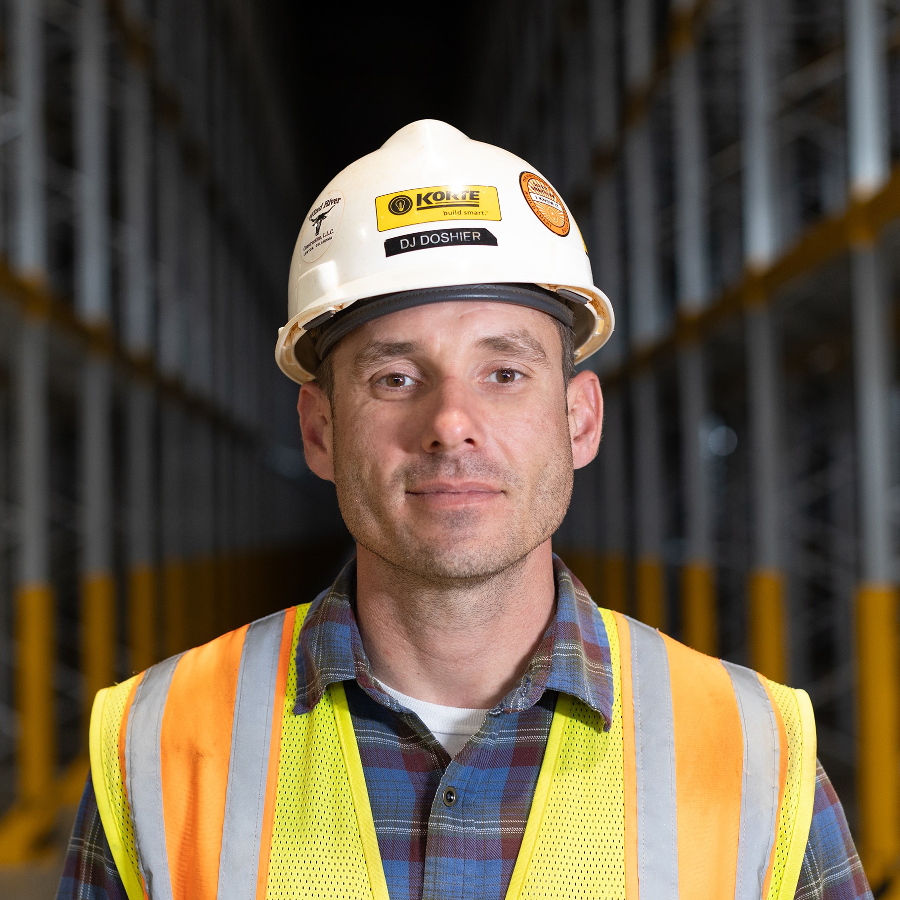 DJ Doshier looking into the camera for a portrait, he is wearing a yellow safety vest and a white Korte hard hat.